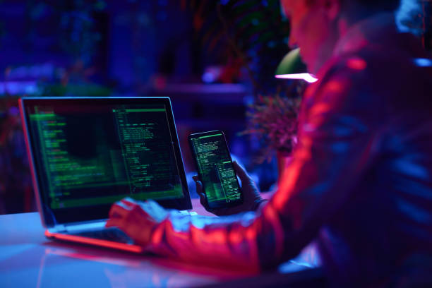Seen from behind modern woman with laptop and smartphone protecting network against cyberattack from hackers on internet in modern office.